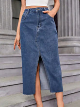 Mid-thigh length medium blue wash midi denim skirt with front slit frayed hem and pockets in denim material