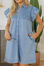 Light blue denim dress with smocked collared neck, puff sleeves, and button-front design