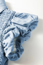 Light blue denim dress with smocked collared neck and gathered ruffled detailing along the shoulder seam