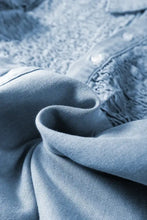 Light blue denim dress fabric with subtle textured weave and visible stitching on smocked collared neck cap sleeve design