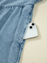 A white iphone 13 peeks from the pocket of a light blue smocked cuffs flared denim shirt mini dress