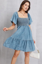 A light blue denim dress with a smocked square neck bodice and tiered skirt perfect for casual wear