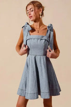A light blue denim dress with a square neckline and diamond bow ribbon tied shoulder bows in a fit and flare style
