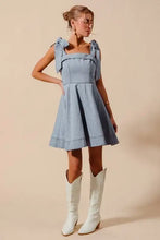 A light blue denim dress with a square neckline and diamond bow ribbon details on the shoulders