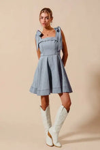 A light blue denim dress with a square neckline and diamond bow ribbon details on the shoulders