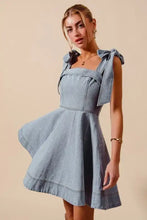 A light blue denim dress with a square neckline and diamond bow ribbon ties at the shoulders