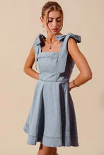 Light blue denim dress with square neckline and tied diamond bow ribbon shoulder bows in a fit and flare style