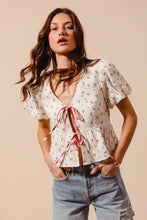 White ditsy floral print gauze blouse with short flutter sleeves and v-neckline tied with red ribbon at front