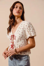 A white ditsy floral print gauze blouse with puff sleeves and v-neckline tied with a red ribbon at the front