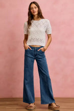 A woman wears blue so me mid rise stretch denim jeans paired with a white short-sleeved knit top with lace detailing