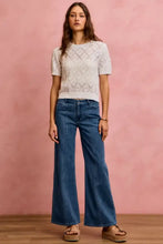 A woman wears white short-sleeved knit top with diamond lace design paired with mid rise stretch denim jeans