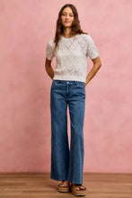 White lace-knit short-sleeved top with diamond pattern paired with mid rise stretch denim jeans in classic blue denim