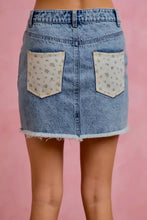 Back view of so me washed denim mini skirt with light wash, floral contrast pockets, and a frayed hem