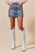 White cowboy boots with embossed floral patterns paired with a washed denim mini skirt with pockets