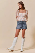 White cowboy boots with embossed detailing and light brown block heels paired with a washed denim mini skirt
