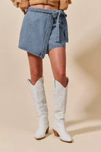 Light blue denim skort featuring a wrap braided trimmed design with a braided belt tied at the waist