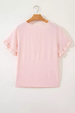 Soft pink short sleeve blouse with delicate ruffle trim cuffs and round neckline displayed on wooden hanger