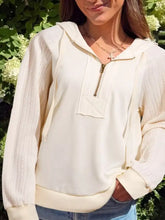 Cream-colored half zip hoodie with ribbed knit sleeves and a small patch pocket made of slightly stretchy material