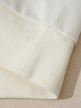 Cream-colored ribbed knit fabric cuff with soft texture on solid color textured sleeve patchwork half zip hoodie made of slightly stretchy material