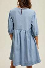 A light blue denim dress with square neck half sleeves puffed sleeves and a gathered waist for machine wash cold care