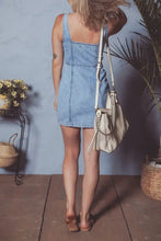 Beige leather crossbody bag with studded detailing and drawstring closure paired with square neck wide strap denim dress