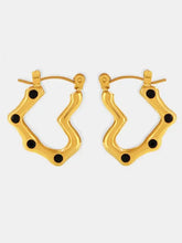 Gold-toned wavy hoop earrings with black enamel dots and stainless steel heart design
