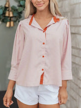 A pink and white striped color block blouse with orange trim and frilled collar button down shirt detail