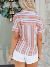 A woman wears a striped button short sleeve shirt with vertical stripes in peach white and pink shades