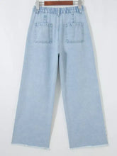 Light blue denim wide-leg jeans with elastic waistband, slit leg frayed hems, and studded pockets for a relaxed fit