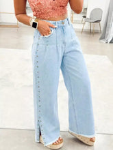 Light blue denim wide-leg jeans with front slit leg frayed and decorative silver studs along the side seam