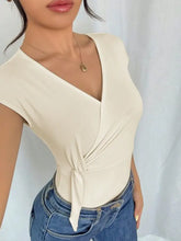 Cream-colored surplice cap sleeve bodysuit with v-neckline and tied waist detail in wrap-style design