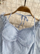 Swiss dot flounce sleeve blouse in light blue with ruffled neckline, tie-back straps, and white floral embellishments