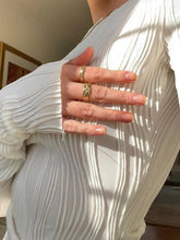 A hand wearing two gold rings resting on a textured long sleeve fitted blouse in soft fabric