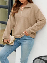 Woman in textured quarter zip long sleeve sweatshirt with beige handbag