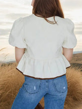 Cream-colored tie-front blouse with puff sleeves and peplum hem accented by brown trim in puff sleeve peplum style