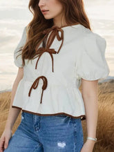 Off-white puff sleeve peplum blouse with cropped fit and brown fabric ties at neckline and waist