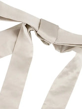 Beige satin ribbon tied into a bow on the tie shoulder of a white satin tie-shoulder satin cami