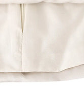 Cream-colored white satin tie shoulder camisole with soft texture, subtle ruffle detail, and matching zipper closure