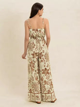 Woman in tie strap wide leg jumpsuit with cream fabric and brown floral patterns