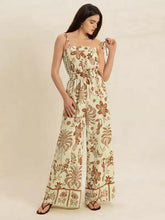 Woman in cream tie strap wide leg jumpsuit with brown botanical prints