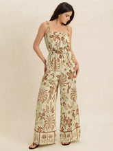 Woman in tie strap wide leg jumpsuit with cream botanical bird patterns