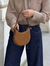 Tan suede crescent-shaped crossbody bag with brown leather straps and gold-tone hardware complements loose fit flare jeans