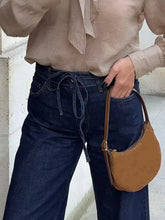 Tan suede crescent-shaped handbag with brown leather handle and gold-tone hardware complements tied loose fit flare jeans