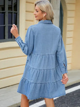 A light blue denim dress with tiered ruffles and long sleeves featuring button up detailing
