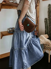 Brown leather crossbody bag with turquoise embellishment on tiered denim maxi skirt