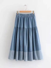 Tiered denim midi skirt with soft blue wash and elastic waistband hanging on wooden hanger for casual wear