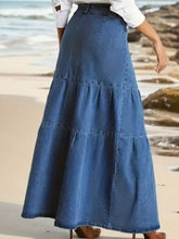 A medium blue wash tiered maxi denim skirt with visible stitching high waistband and zipper detail