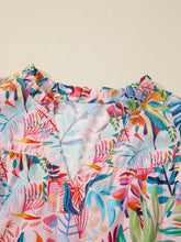 A tropical floral print frilly blouse with a soft pink base featuring colorful leaves and a notched neck design