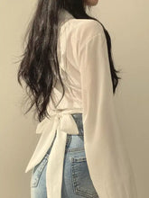 Twisted front long sleeve shirt in flowing white fabric with long sleeves and a tied-back waistband visible from back
