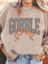 Beige ribbed knit baggy sweatshirt with bold black and white checkered gobble lettering and orange bow, slightly stretchy material and machine wash cold